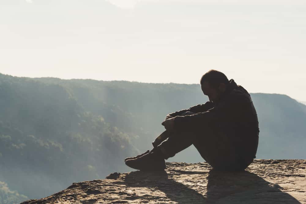 The sad and depressed man sit near the cliff.