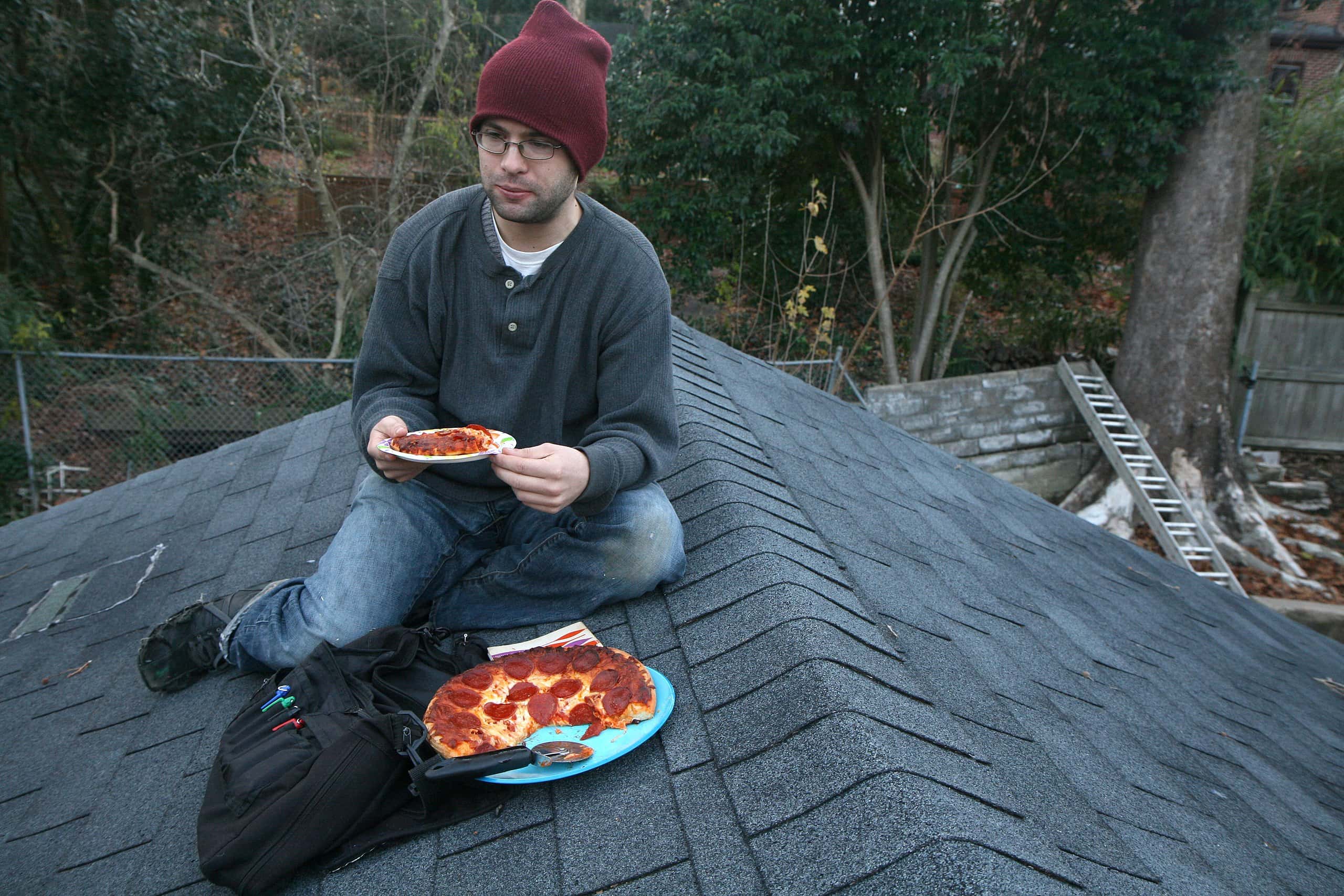 Man eating pizza on a rooftop