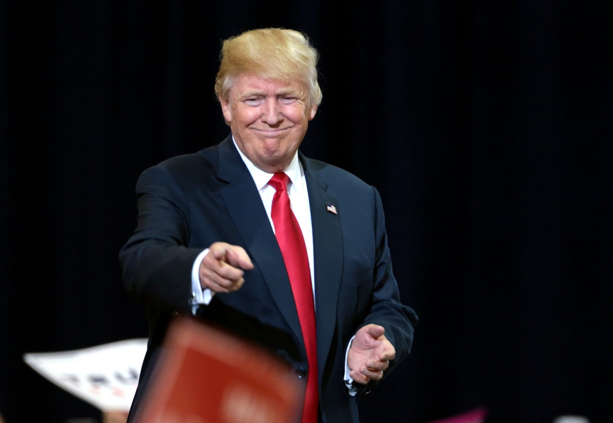 Donald Trump wearing a suit is pointing at front.