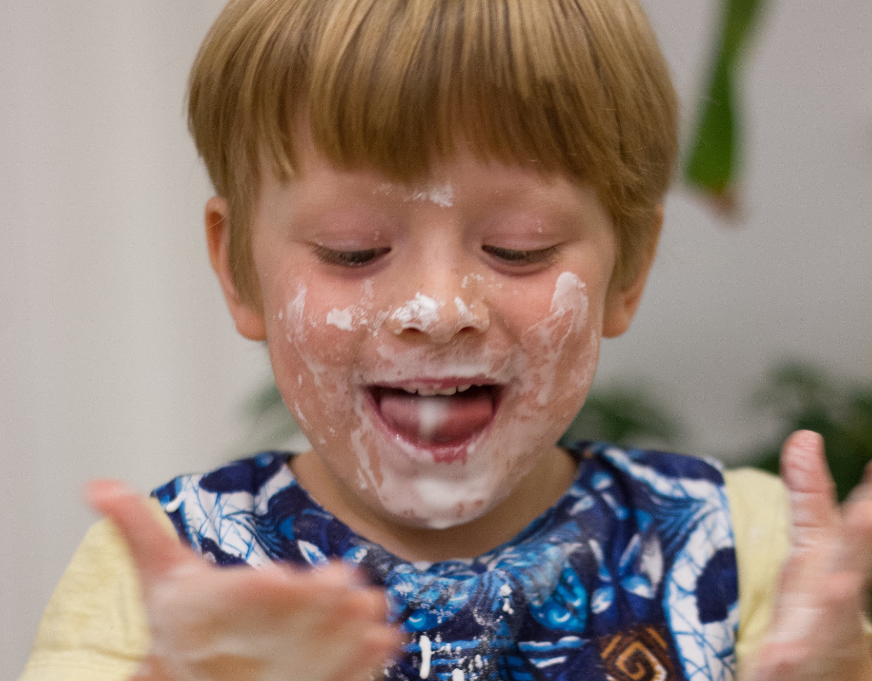 Small kid with white shirt having cake on his face and hands.