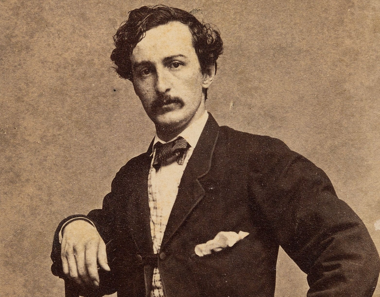  Casual seated pose of John Wilkes Booth with one arm resting on the back of the chair and the other resting on his hip