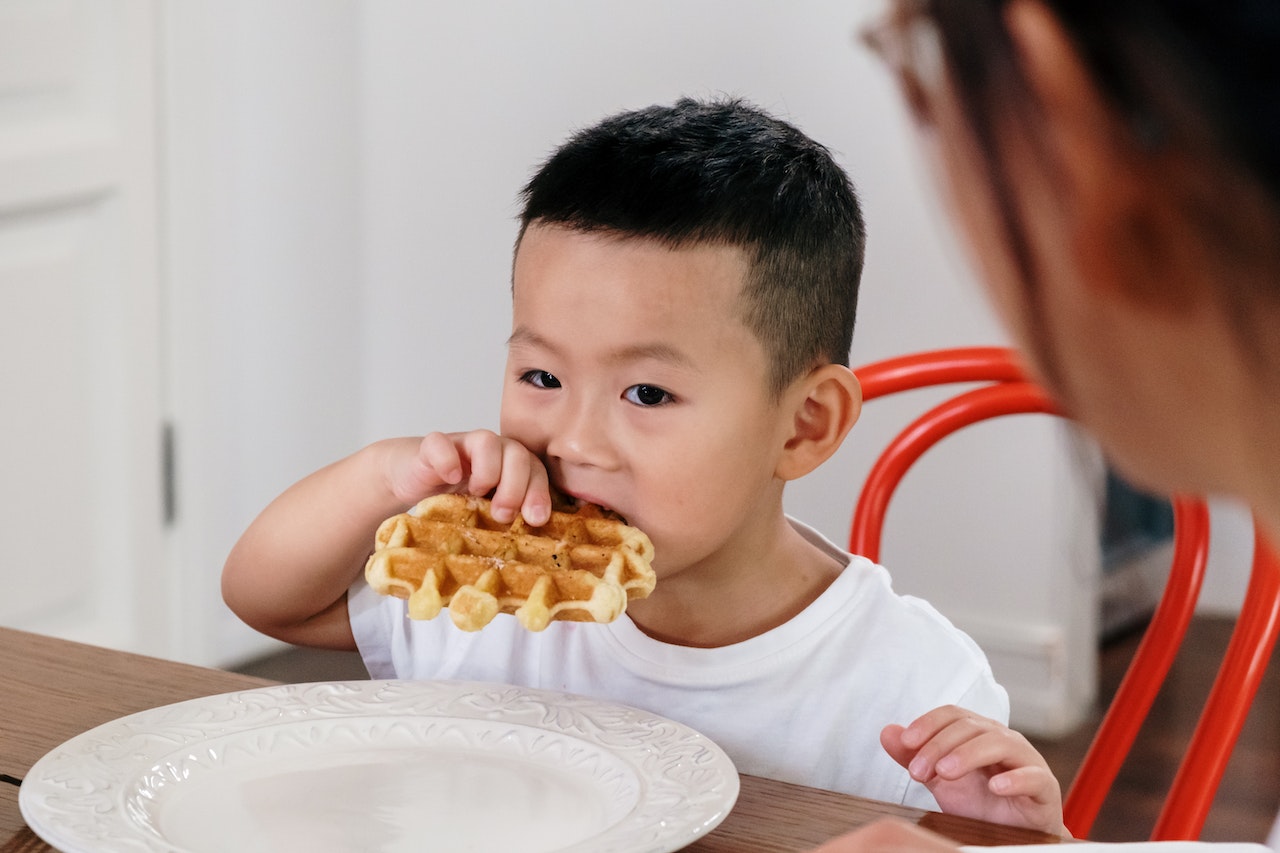 Boy in white t-shirt eating on the table.