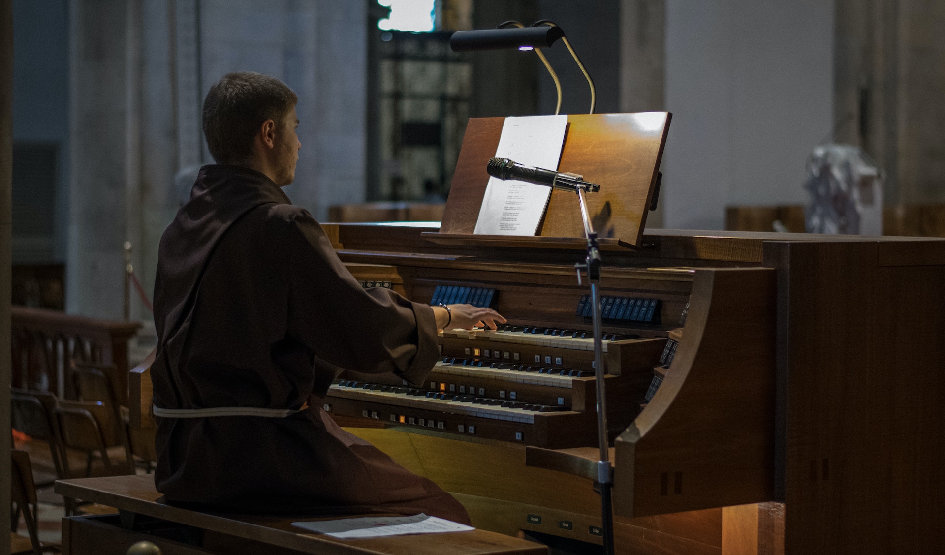 A man in brown long sleeve robe playing on a church organ.