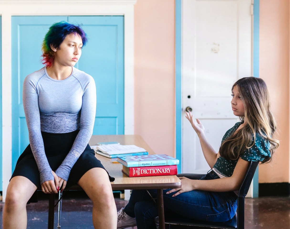 Two girls seating on school bench and talking .