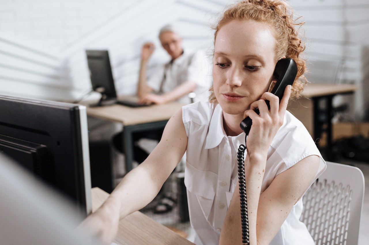 Woman in white shirt talking on telephone in office.