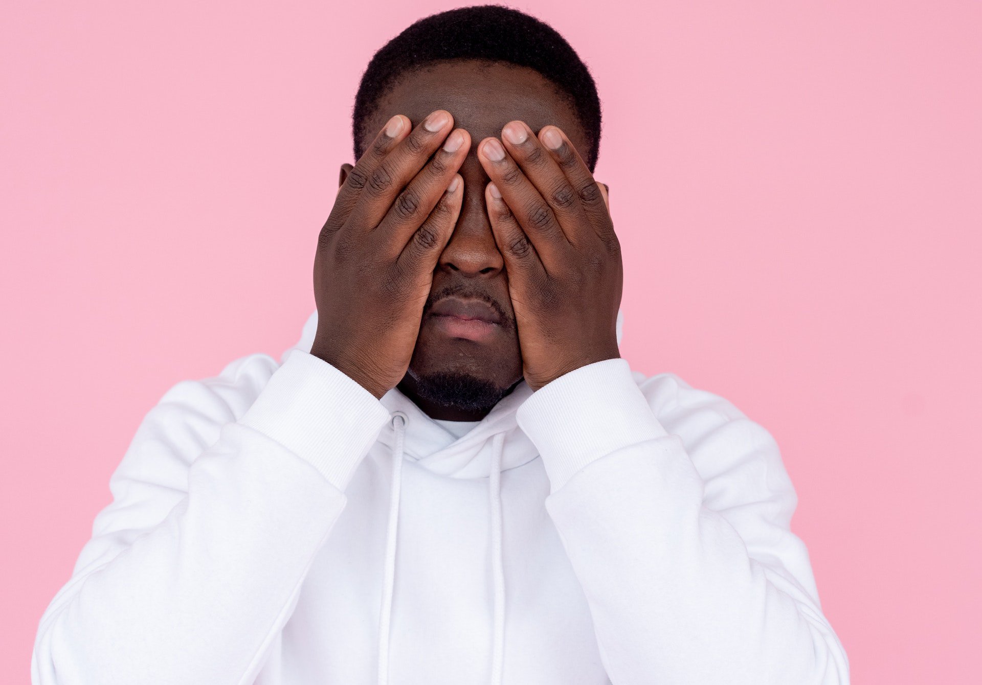 Sad man in white sweatshirt in front of pink background