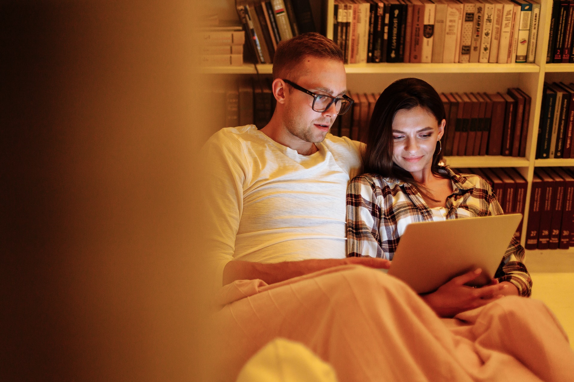 Man and woman sitting on a bed looking at a laptop 
