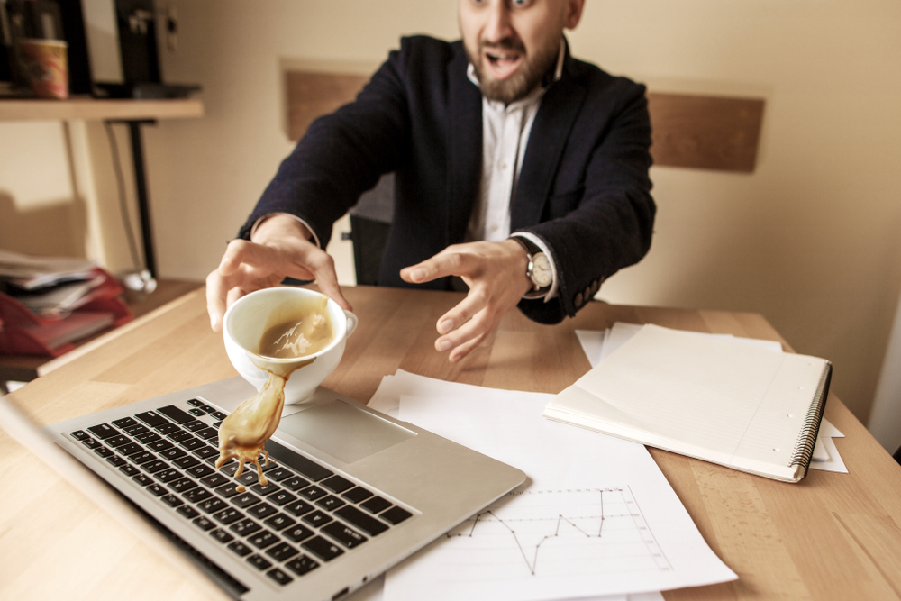 Male employee spills coffee over his laptop