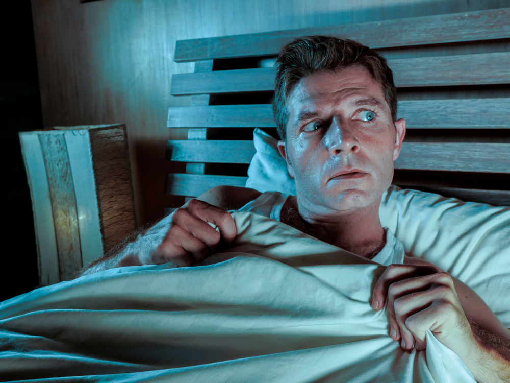 Shocked man lying in bed covered with blanket