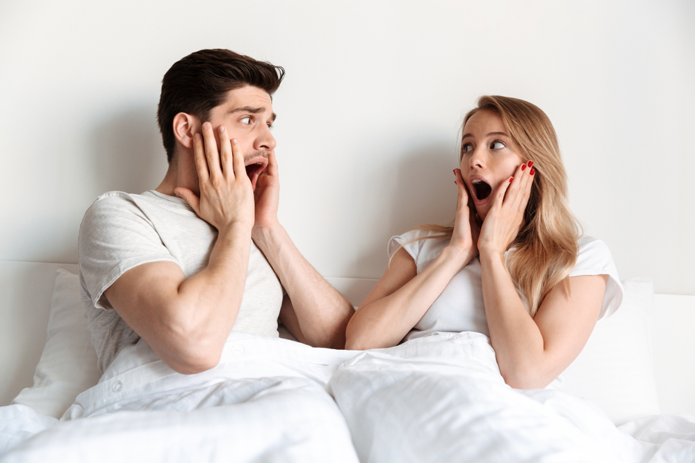 Image of young scared shocked screaming couple lies in bed with mouth opened 