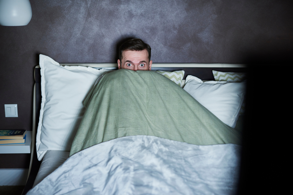 Scared man in bed covered with blankets 