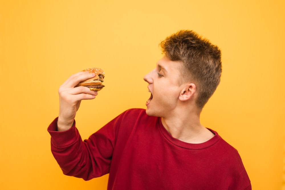 Young man eats fast food in red sweeter