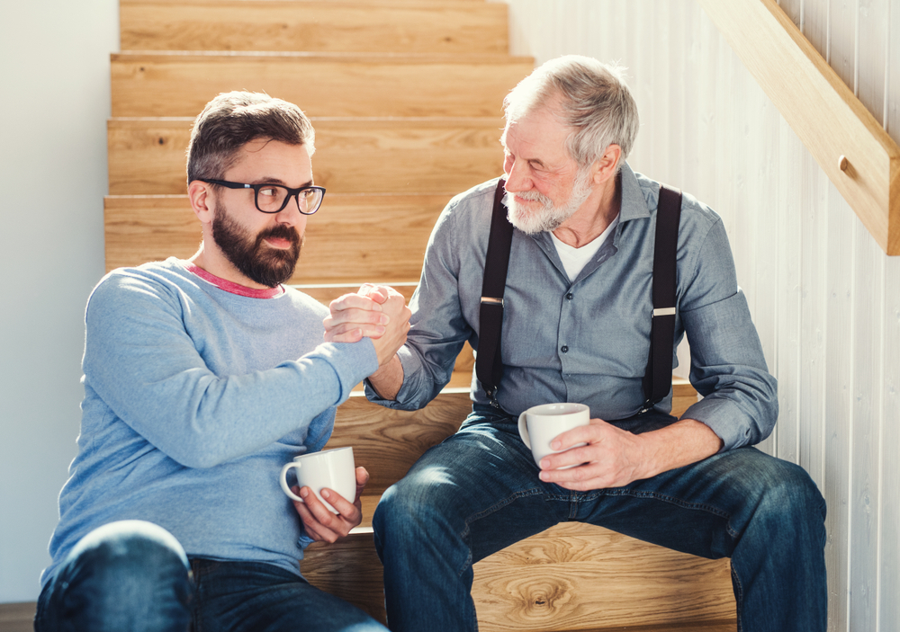 Happy Adult and senor man sitting on stairs drinking coffee