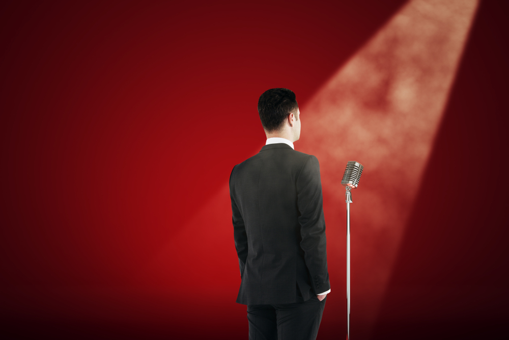 Man giving speech on red background with smoke, mic and spotlight