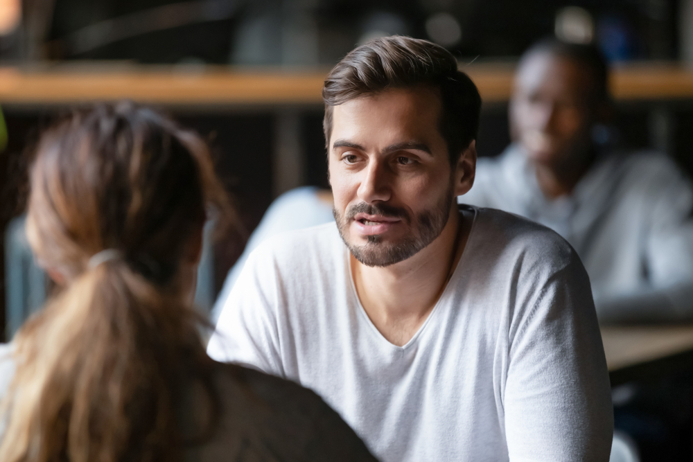 Young serious man having conversation with woman girlfriend sitting at a caffee table