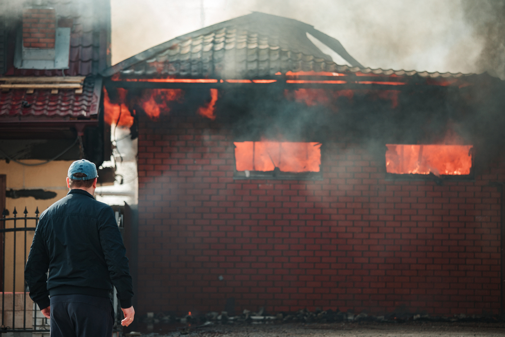 A man stands in front of his burning house and looks with horror