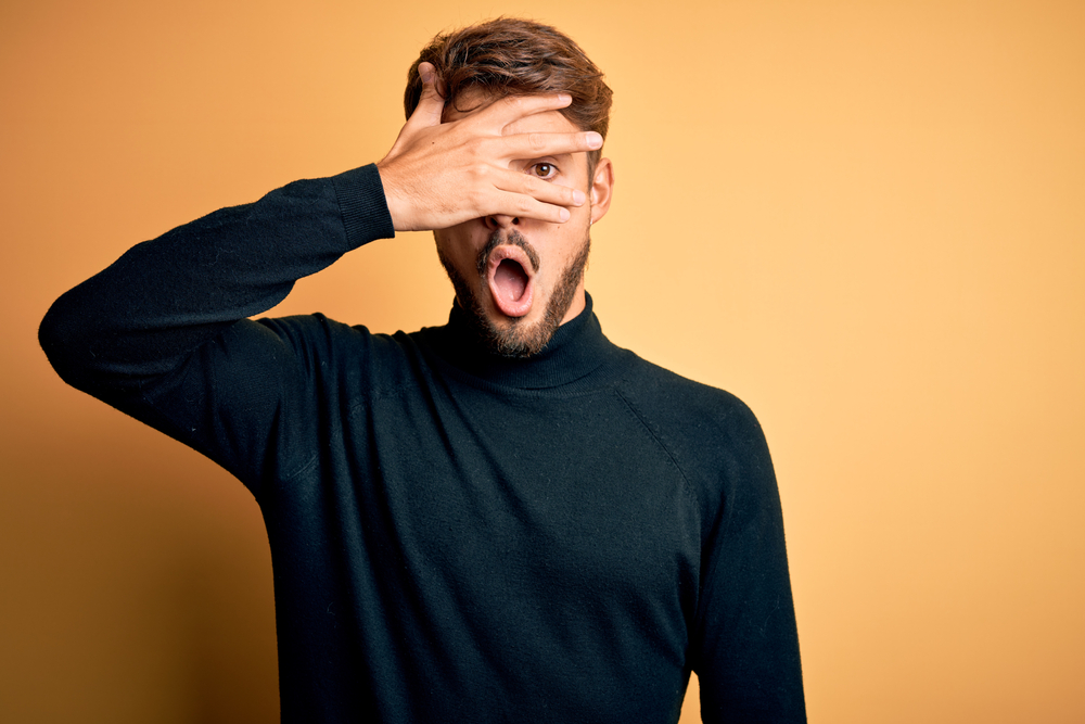 Young handsome man with beard in shock covering face and eyes with hand 