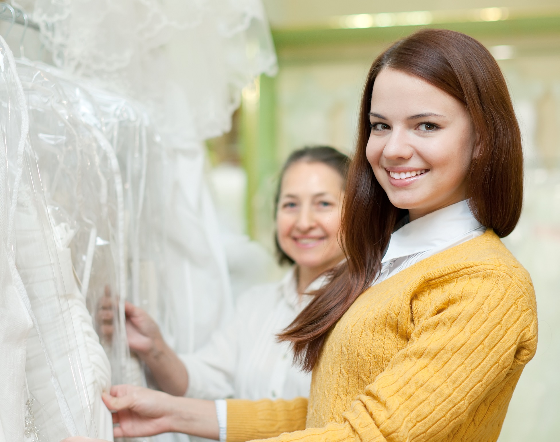 Woman in yellow sweater and white shirt holding a wedding dress smiling.