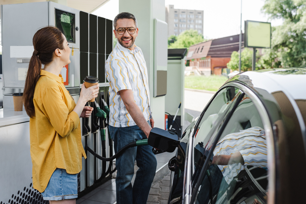 Man and woman at gas station man is filling the car with gas and the woman is drinking coffee