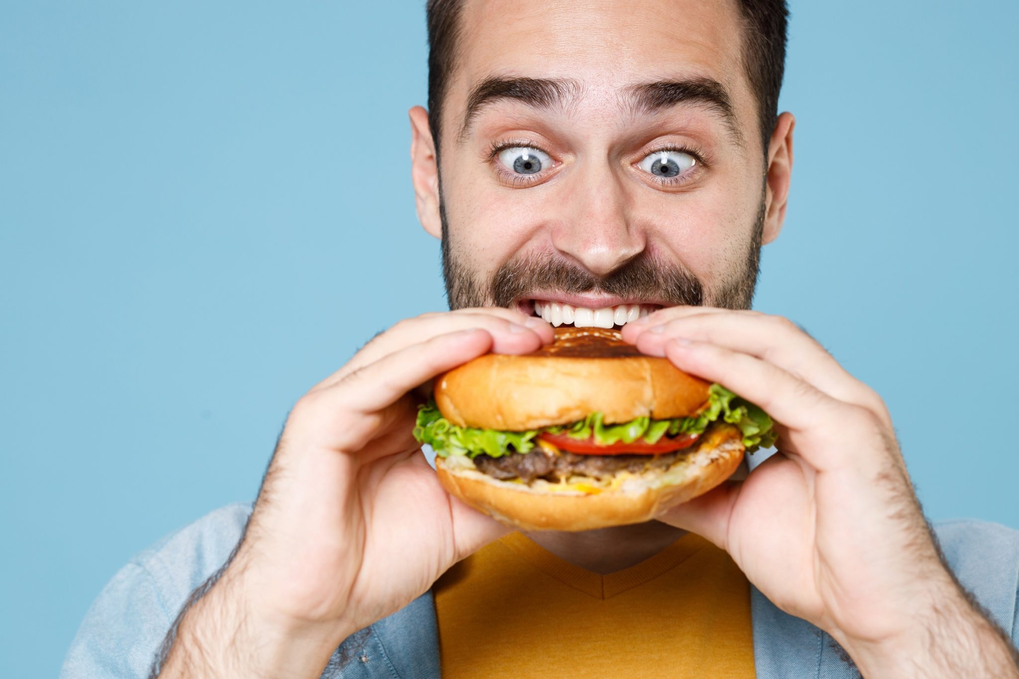 Young bearded man wearing casual clothes eating classic fast food burger.