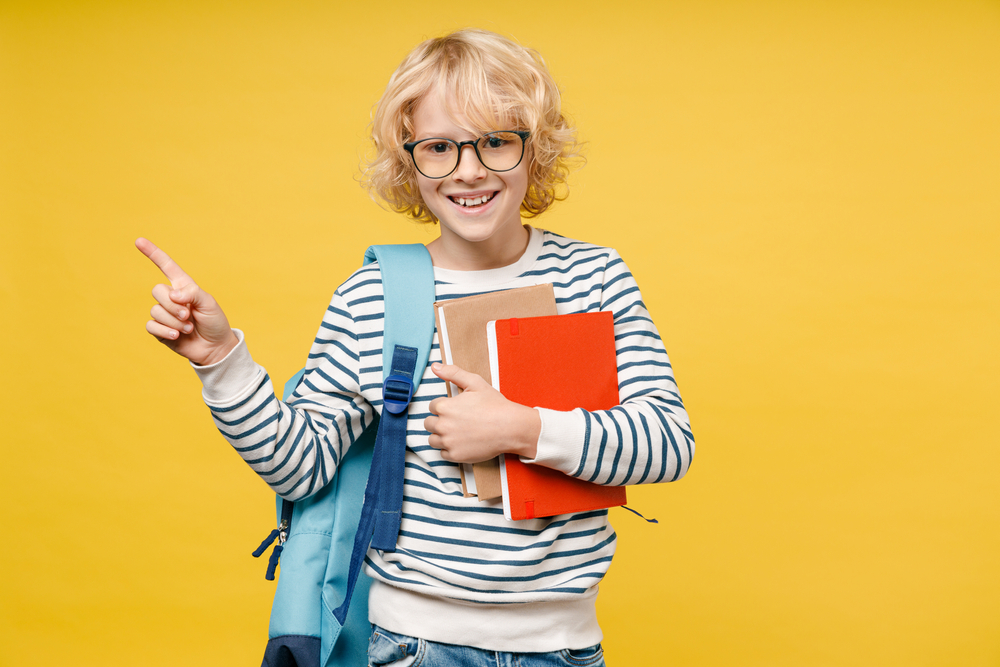 Smiling male kid teen boy 10s years old in striped sweatshirt eyeglasses backpack hold school books point index finger aside up