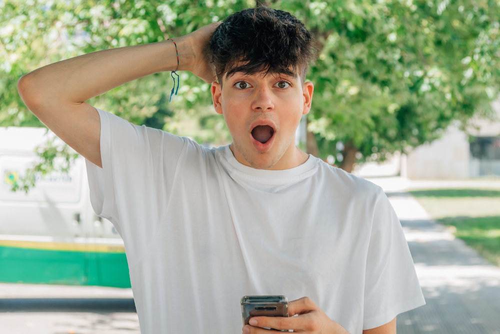 Shocked teenager with one hand on his head holding a phone 