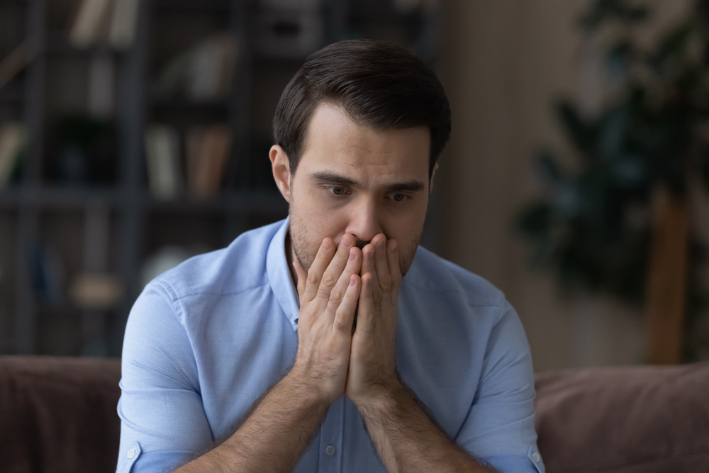 Scared man sitting on a couch with hands over mouth gesture