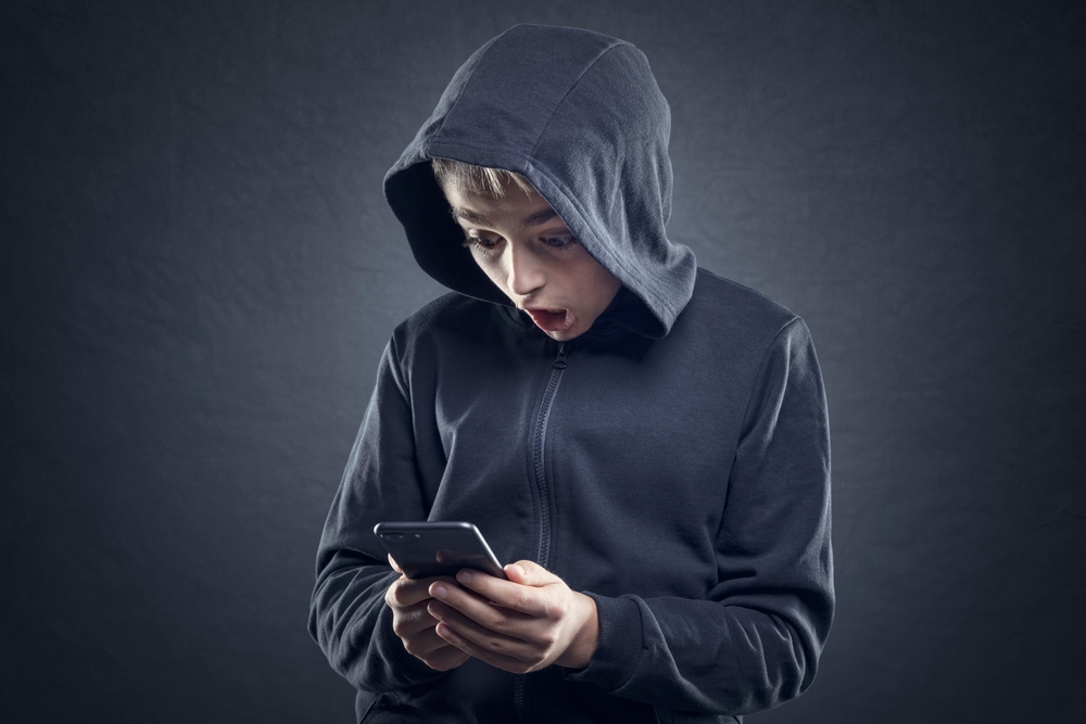 Shocked teenager in gray sweatshirt wearing a hat in front of gray background