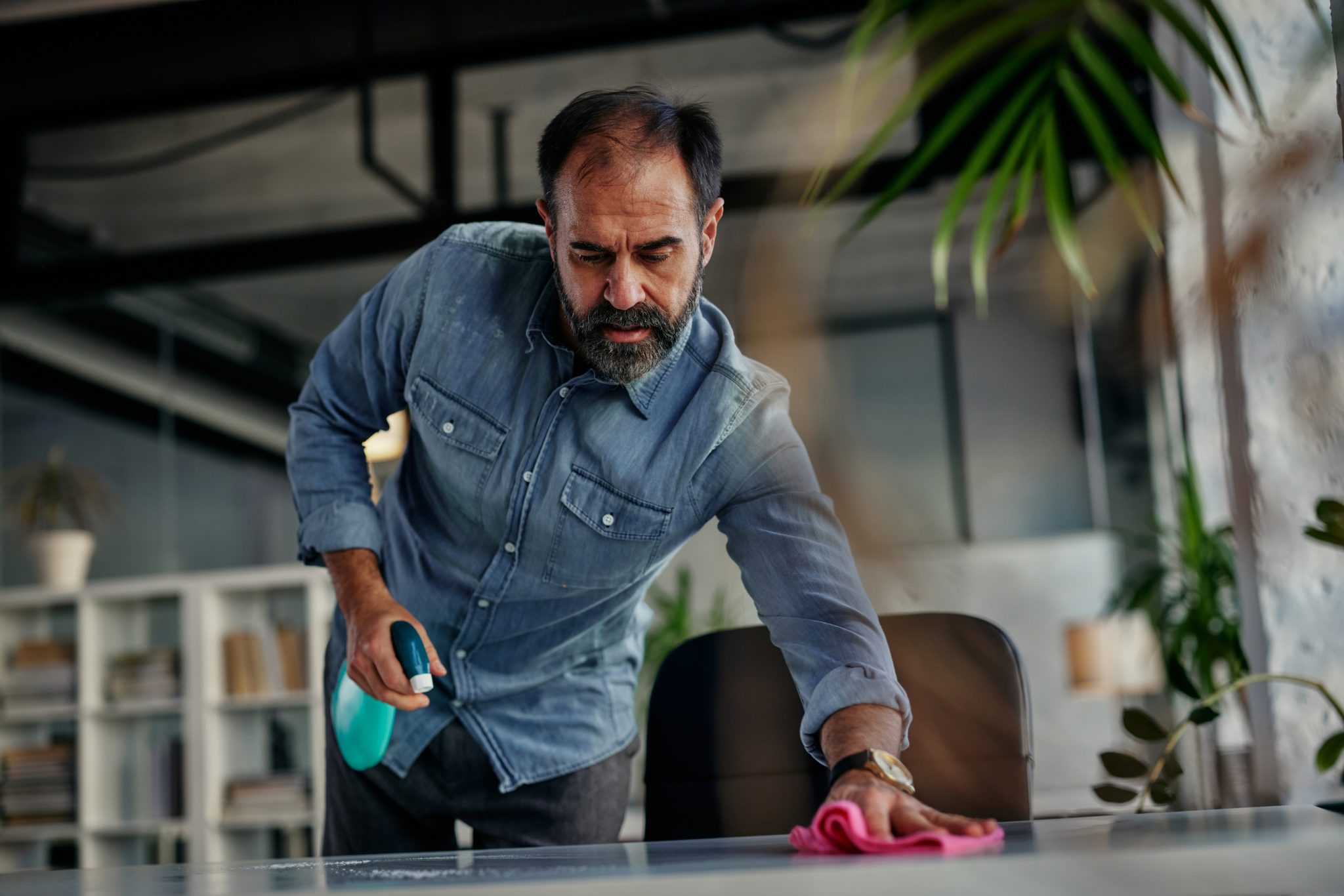 Man in denim shirt cleaning the table with pink cloth.