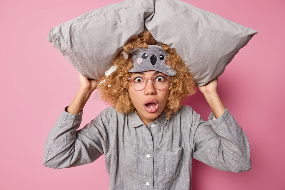 Shocked young woman with curly hair awakes during night after seeing nightmare