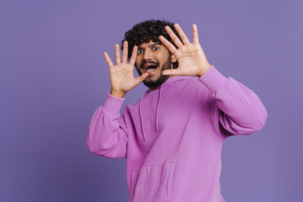 Portrait of young Indian handsome curly haired scared man stretching his arms showing surrender gesture 