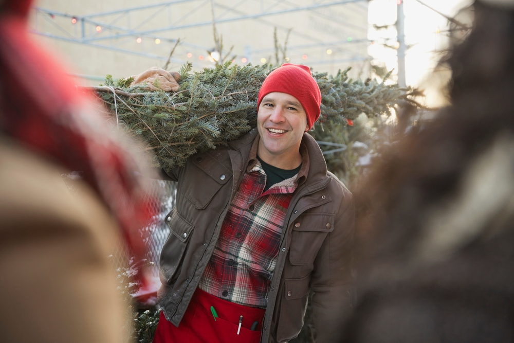 Happy Tree lot owner carrying Christmas tree for customers