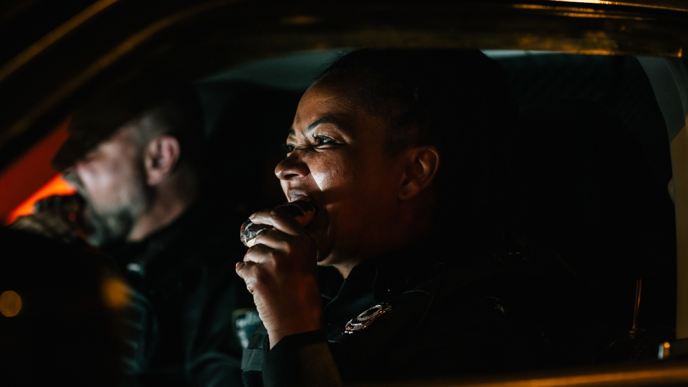 Portrait of Two Police Patrol Officers Sitting in the Car Eating, Watching Over the Streets At Night