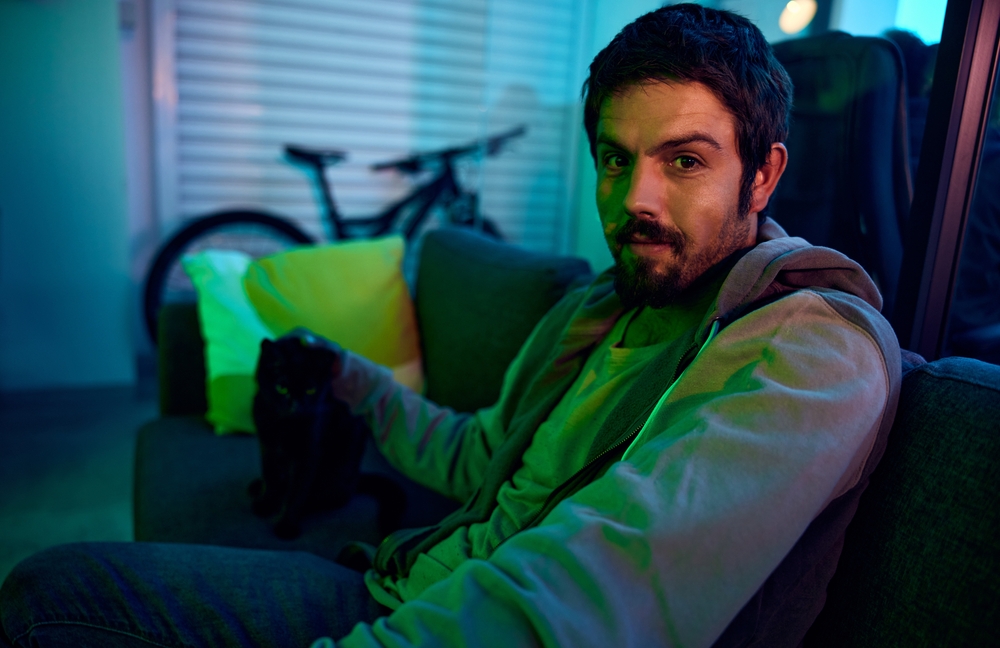 Confused shocked man in living room petting a cat 