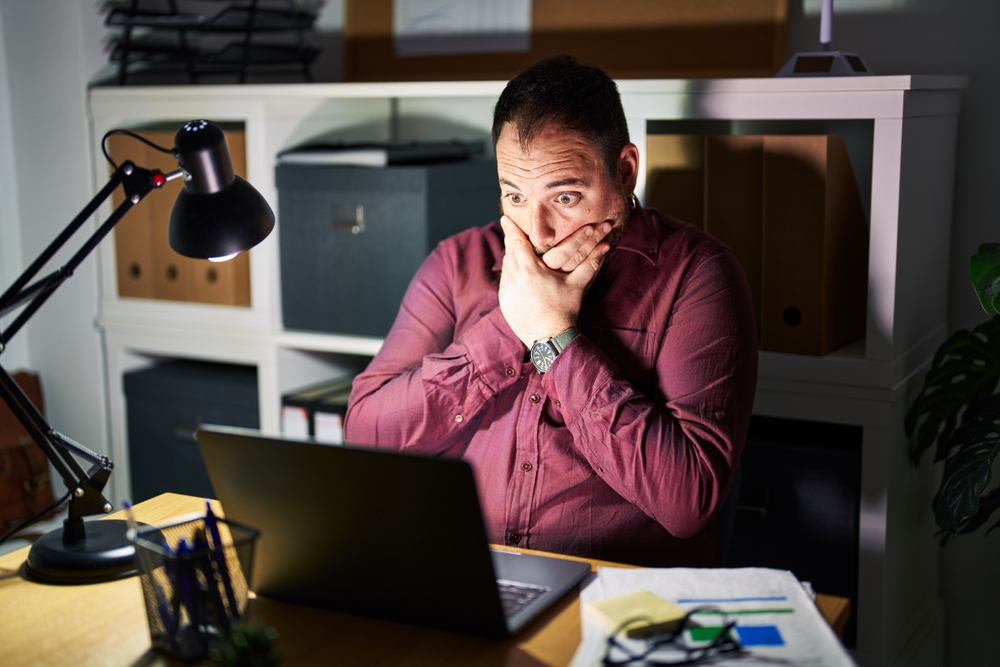 Man working in office shocked covering mouth