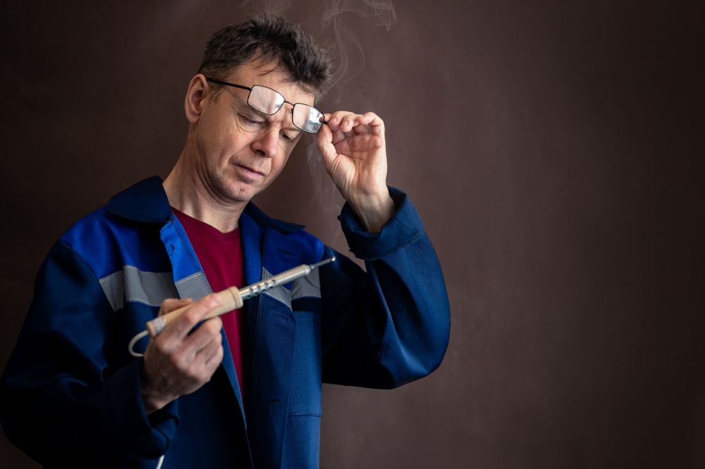 A man with glasses looks at a smoking soldering iron