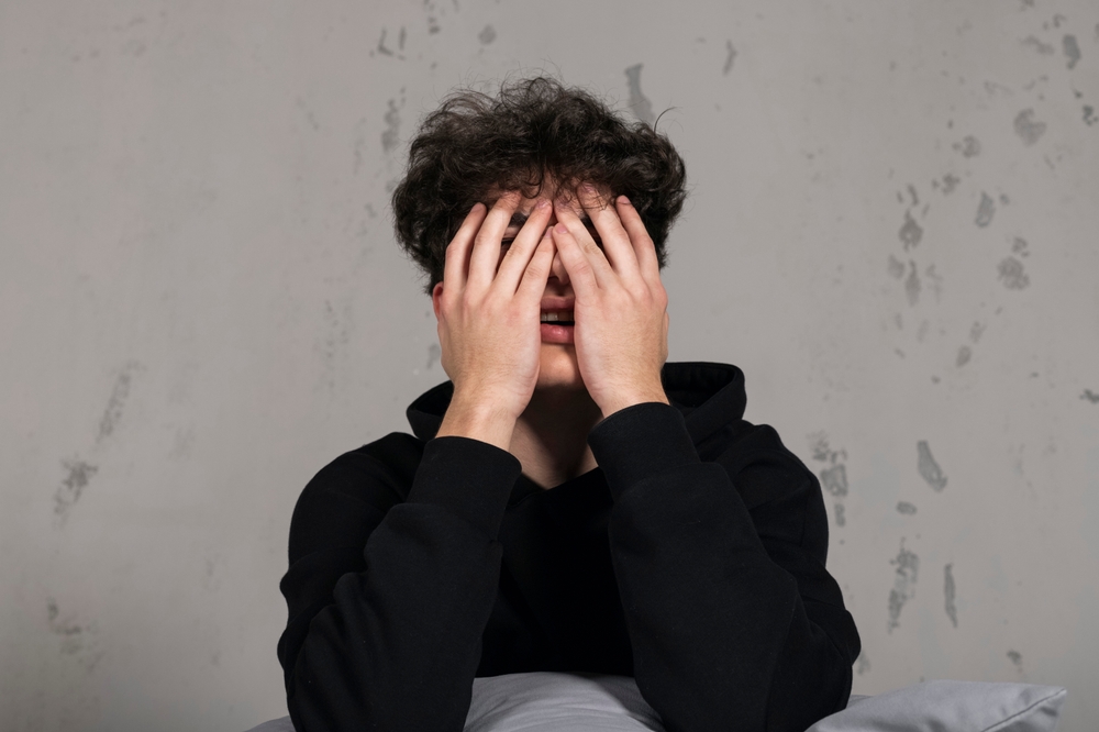 Scared teenager sitting on the bed crying and covering his eyes