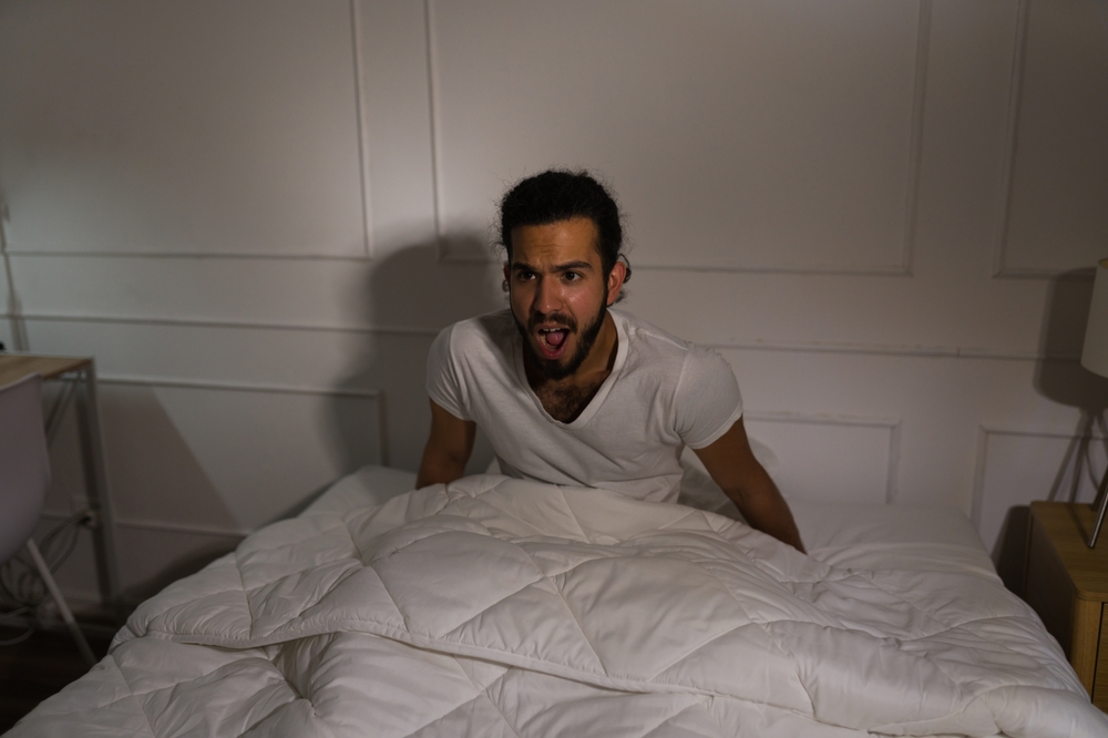 Scared man getting up of bed in white t-shirt 