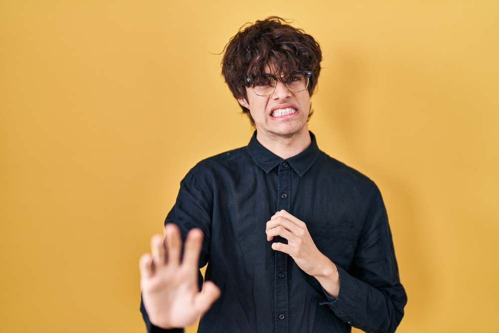 Young man wearing glasses with disgusted expression with raised hands