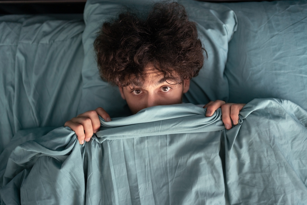Scared man just woke up of bed, covered with blue blanked