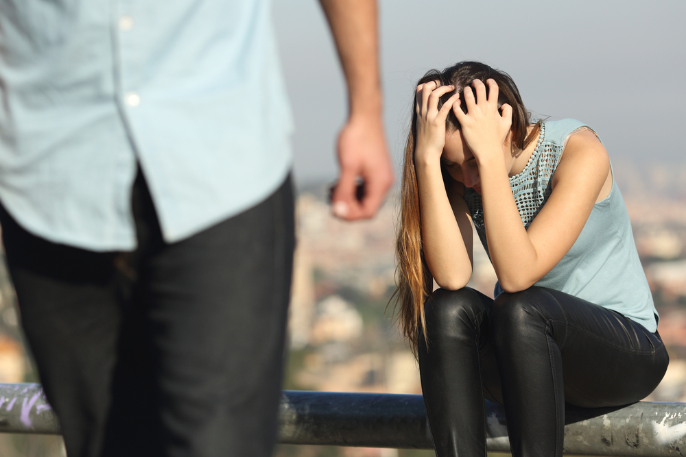 Breakup of a couple, man leaving and sad girlfriend sitting on a fence covering her face with hands