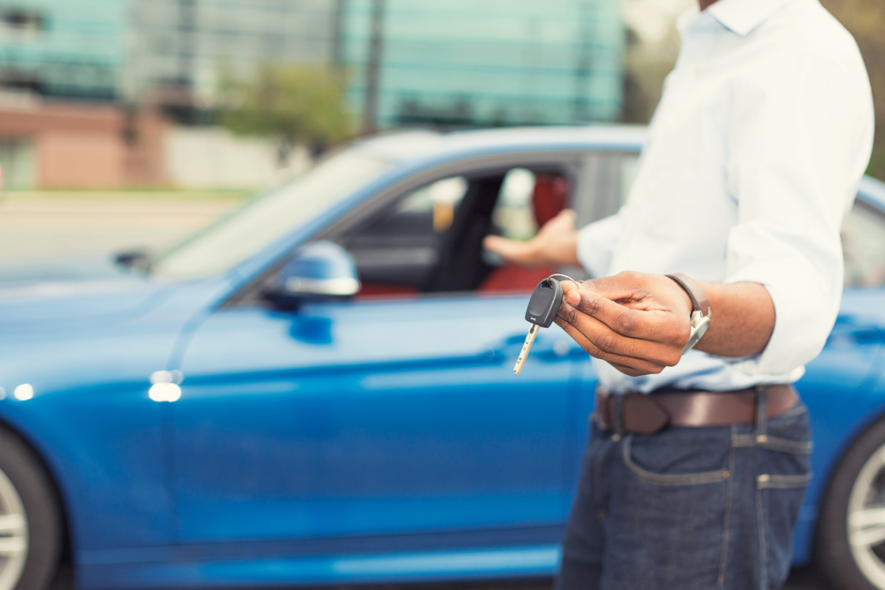 Male hand holding car keys offering to sell new blue car