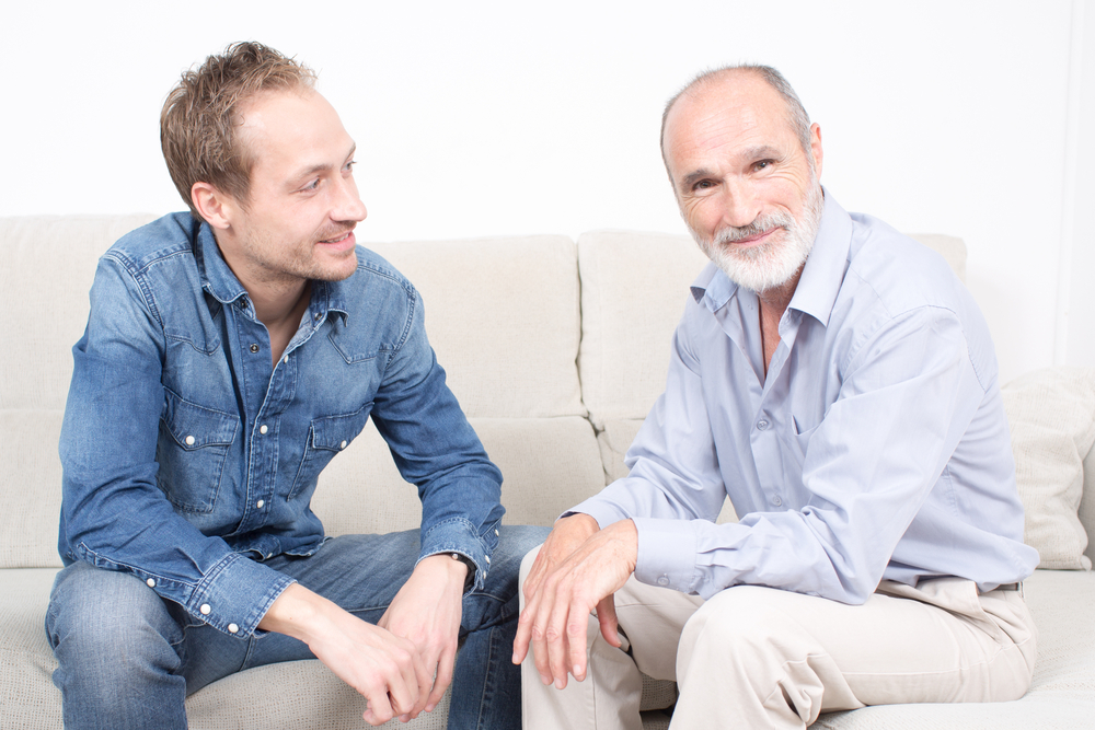 Two men talking, older and younger , sitting on a couch