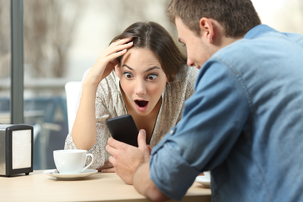 Shocked couple at coffeeshop looking at phone