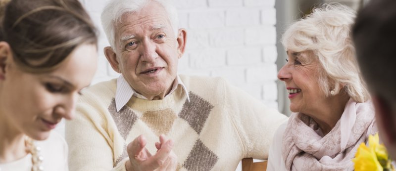 Older happy man sitting with his wife during family dinner