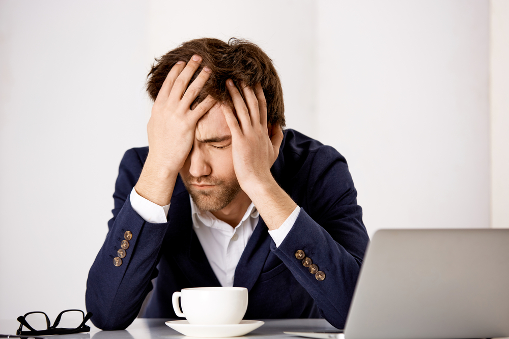Portrait of a young handsome businessman in suit sitting shocked at office at the desk