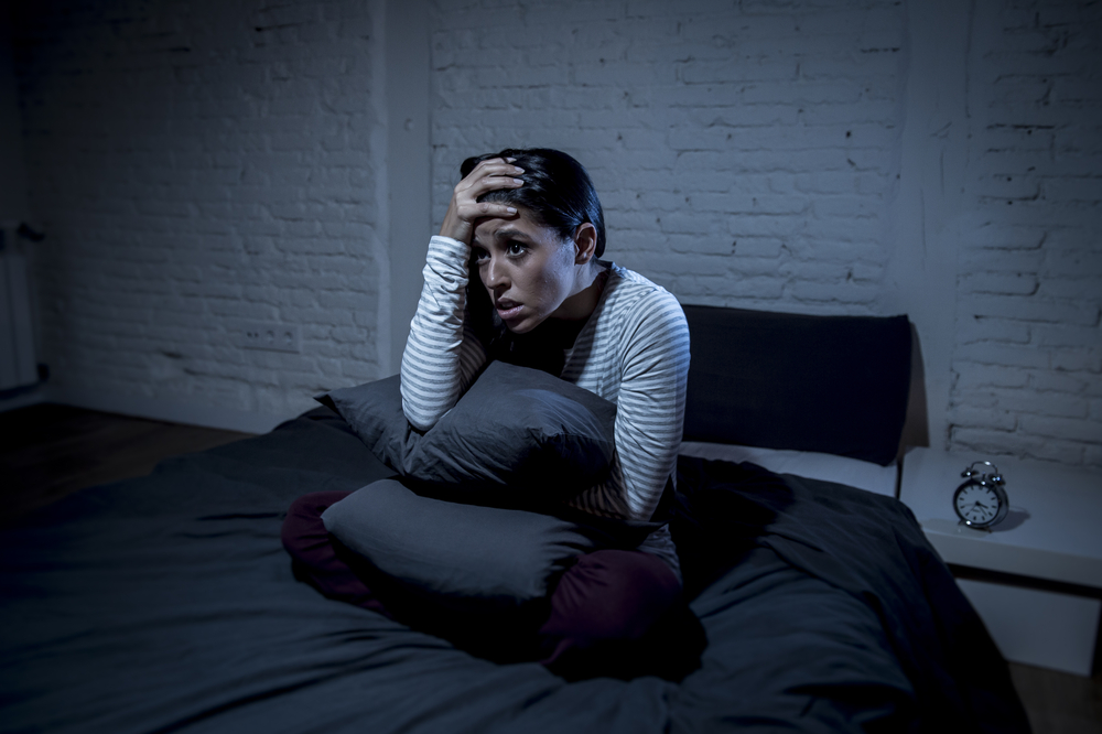 Scared woman sitting in bed hugging a pillow