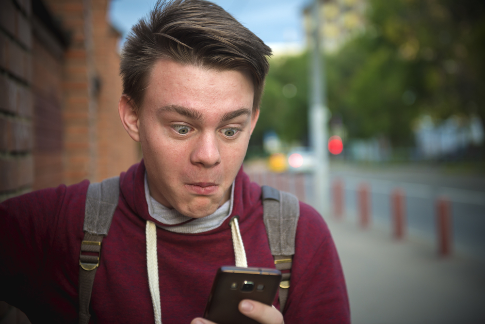 Shocked teenager looking at phone with eyes wide open 