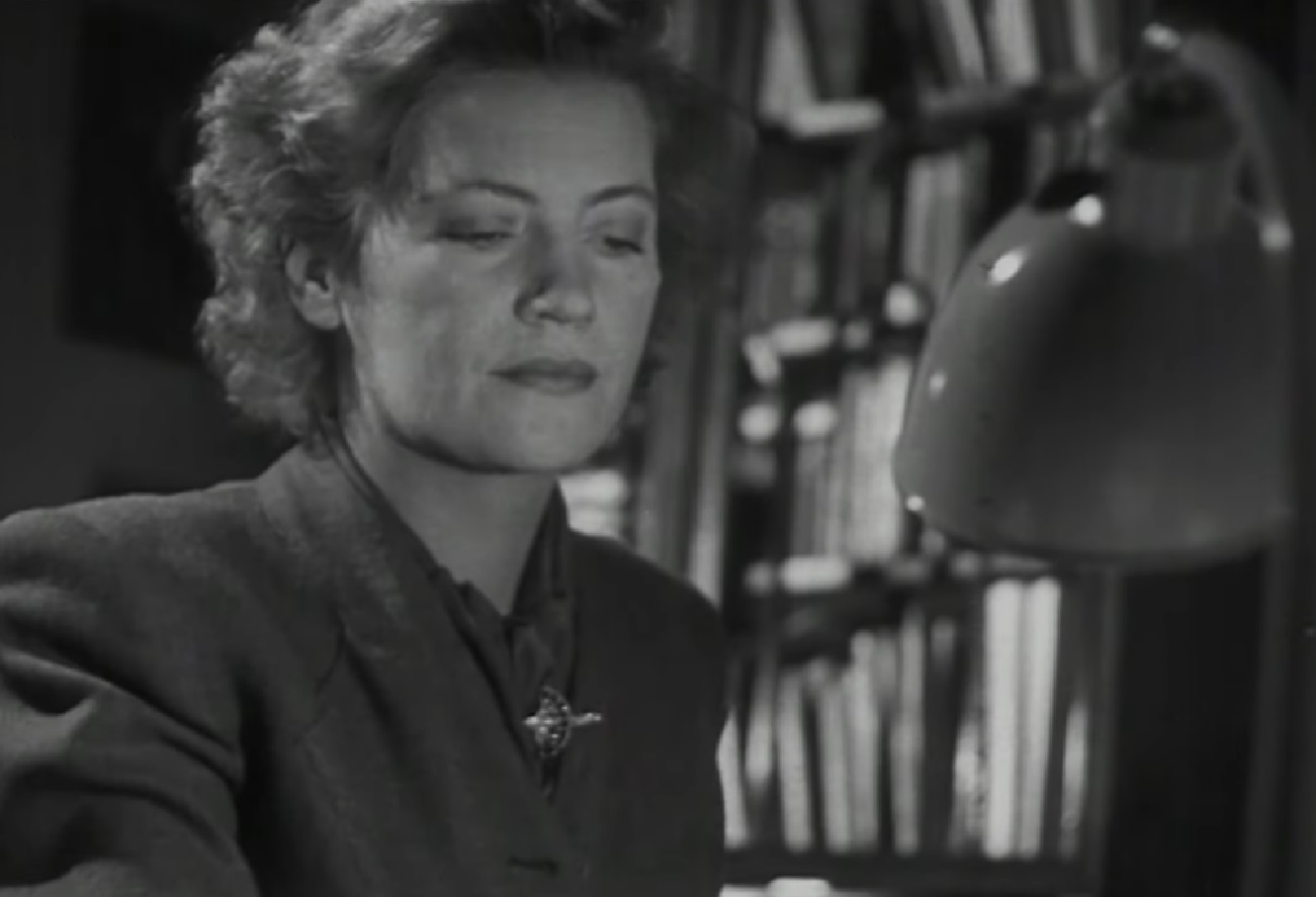 Screenshot: B&W Lee Miller seating on desk and looking down - from Lee Miller- Through The Mirror (1955)