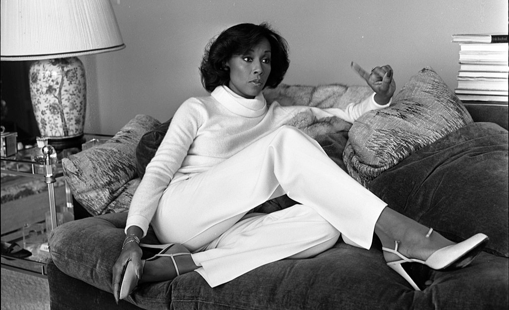 Grayscale photo of the actress Diahann Carroll siting on a couch wearing white clothes